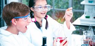 La imagen muestra a dos estudiantes en un laboratorio realizando experimentos con implementos científicos