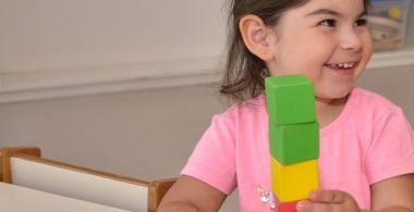 La imagen muestra a una niña pequeña jugando con unos cubos de colores