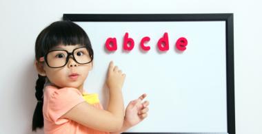 La imagen muestra a una niña indicando unas letras en una pizarra